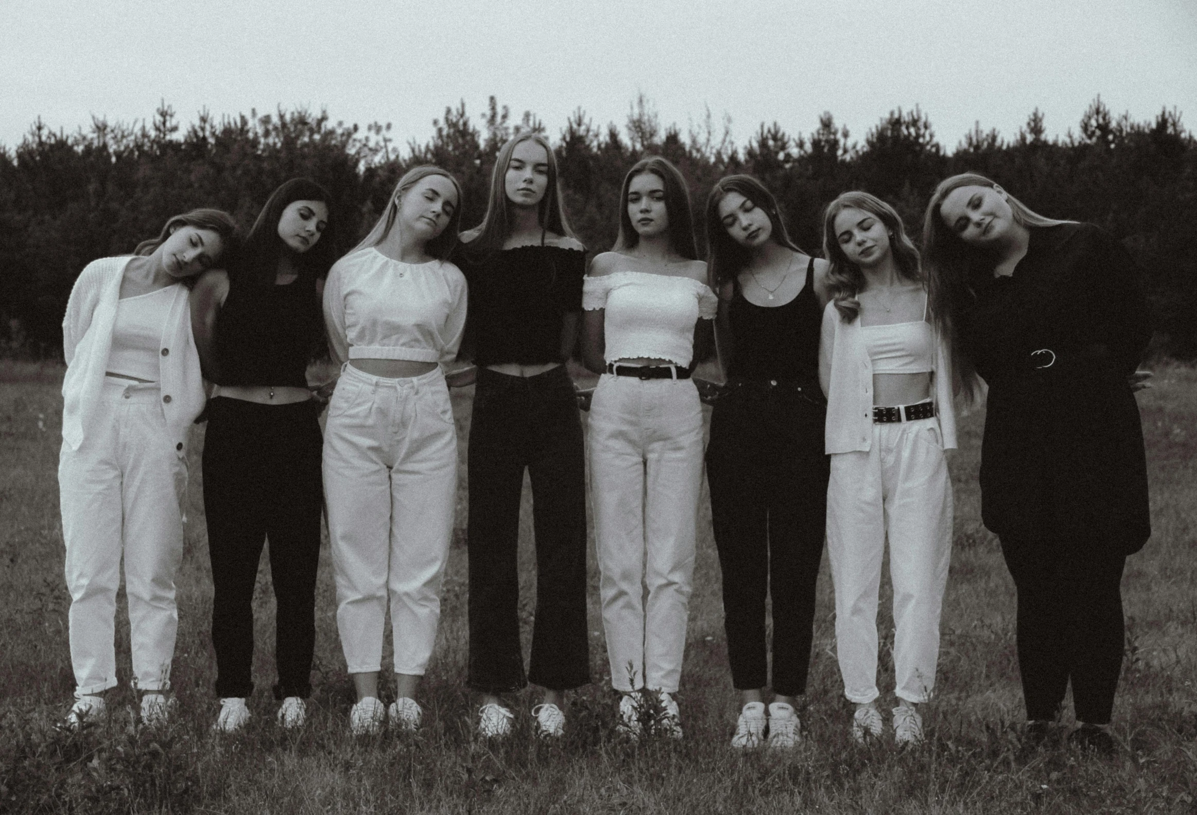 a group of women standing next to each other in a field, an album cover, trending on pexels, antipodeans, white and black clothing, standing in a dimly lit room, high school girls, group of seven