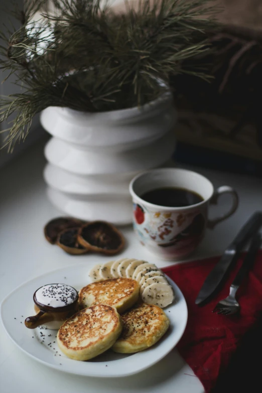 a white plate topped with pancakes next to a cup of coffee, a still life, by Lucia Peka, pexels contest winner, winter, banana, thumbnail, ukrainian