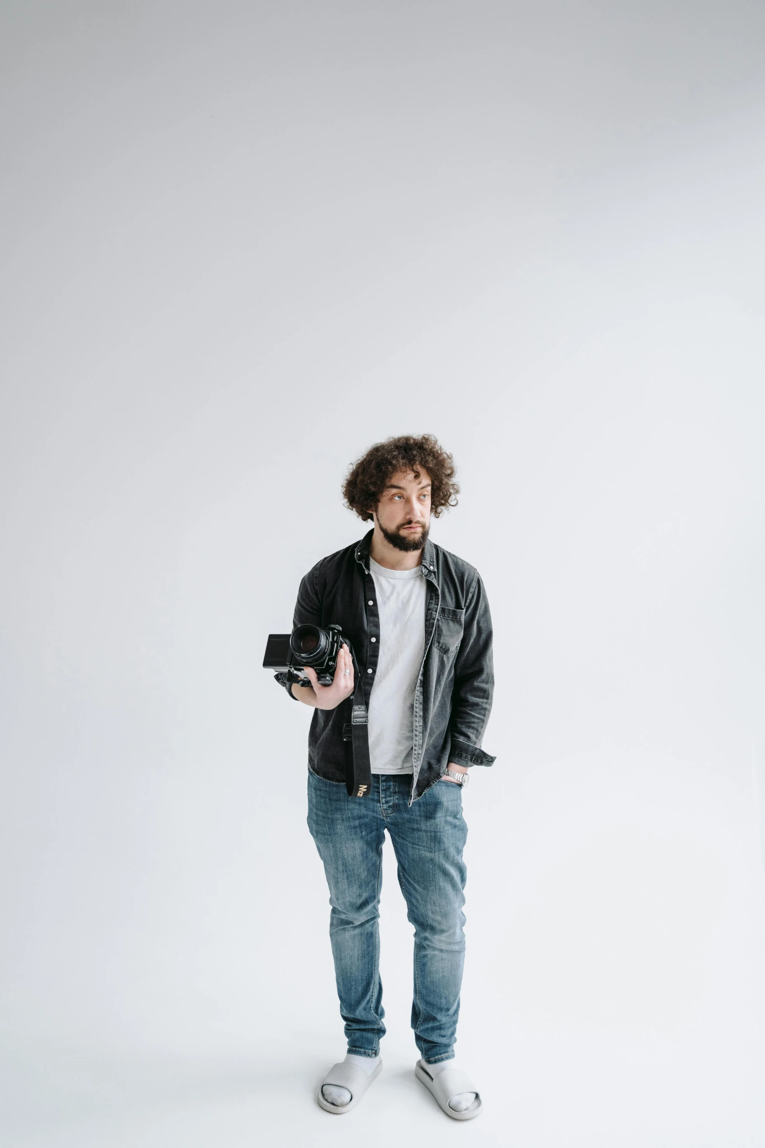 a man standing in front of a white background, unsplash contest winner, photorealism, curly haired, holding a dslr camera, scruffy man, giorgio a. tsoukalos