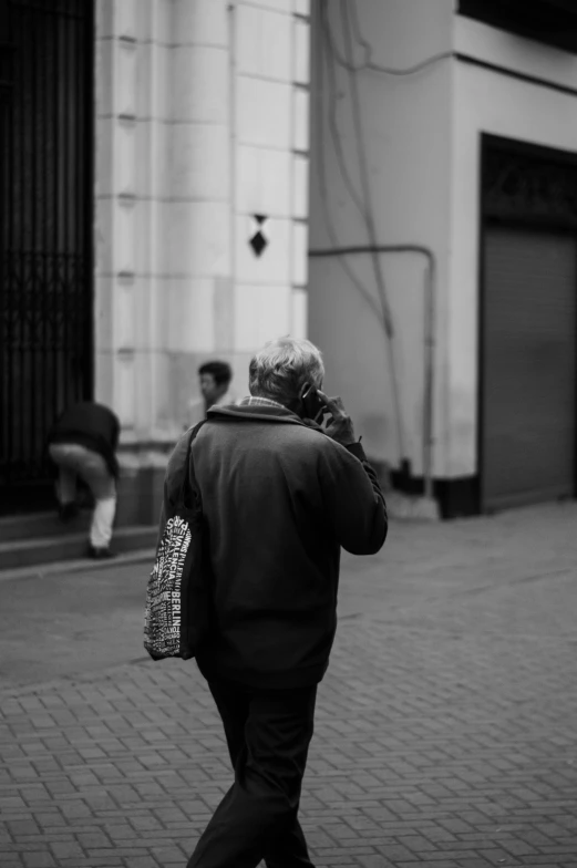 a black and white photo of a woman walking down the street, by Altichiero, looking at his phone, old male, with his back turned, telephhoto