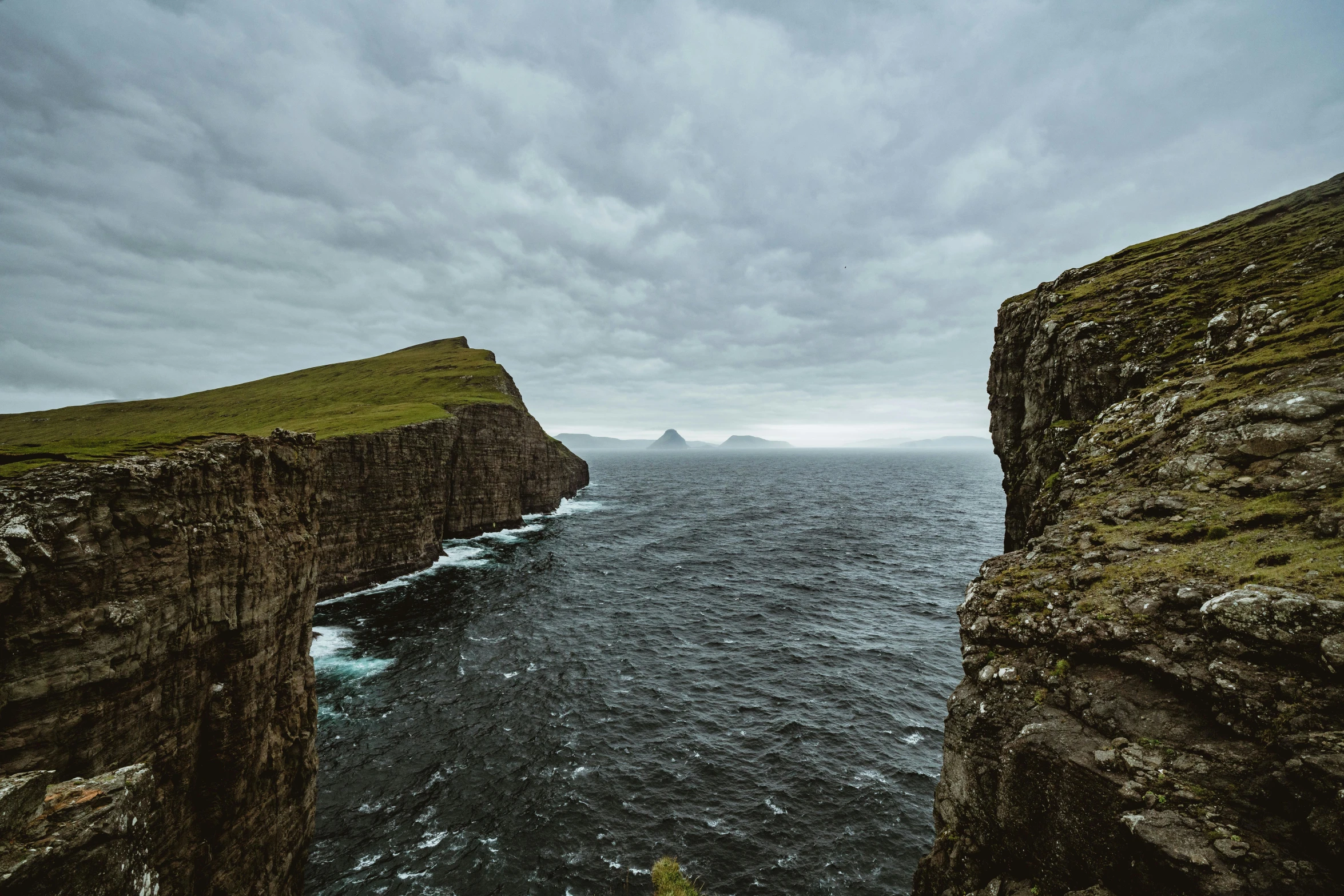 a man standing on top of a cliff next to the ocean, by Matthias Stom, pexels contest winner, faroe, erosion algorithm landscape, two medium sized islands, overcast skies