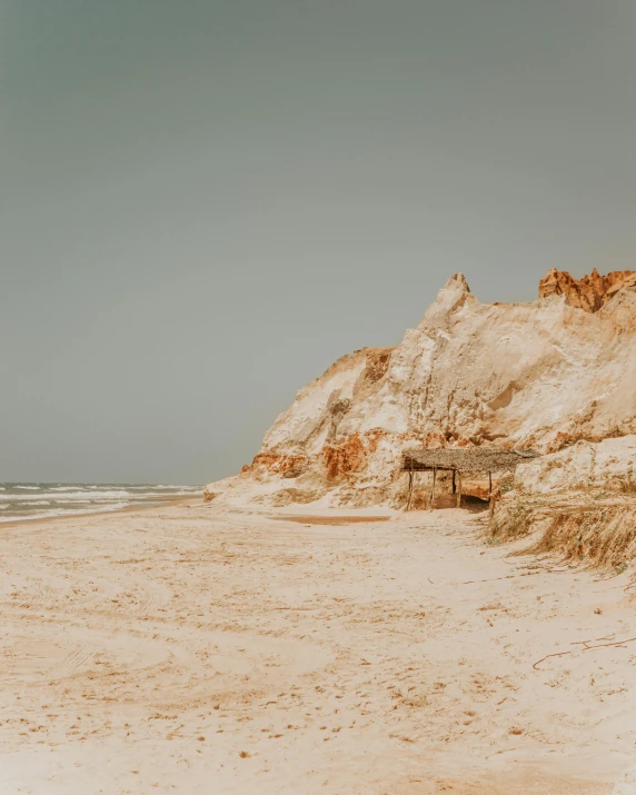 a man standing on top of a sandy beach next to the ocean, by Kristian Zahrtmann, unsplash contest winner, australian tonalism, sand - colored walls, white rocks made of bone, the village on the cliff, on a canva