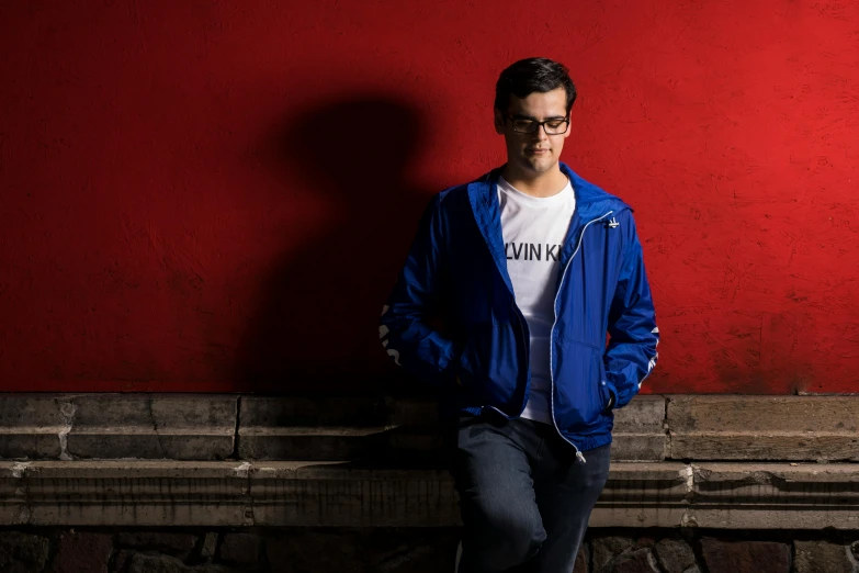 a man in a blue jacket leaning against a red wall, pexels contest winner, hyperrealism, magnus carlsen, angry video game nerd, photo from a promo shoot, clothed in ancient street wear