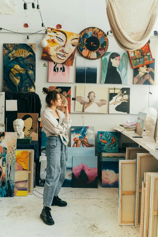 a woman standing in front of a bunch of paintings, trending on pexels, arbeitsrat für kunst, girl in studio, etsy, profile pic, art station ”