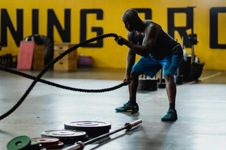 a man holding a rope in a gym, by Robbie Trevino, pexels contest winner, yellow and black color scheme, athletic crossfit build, profile image, thumbnail