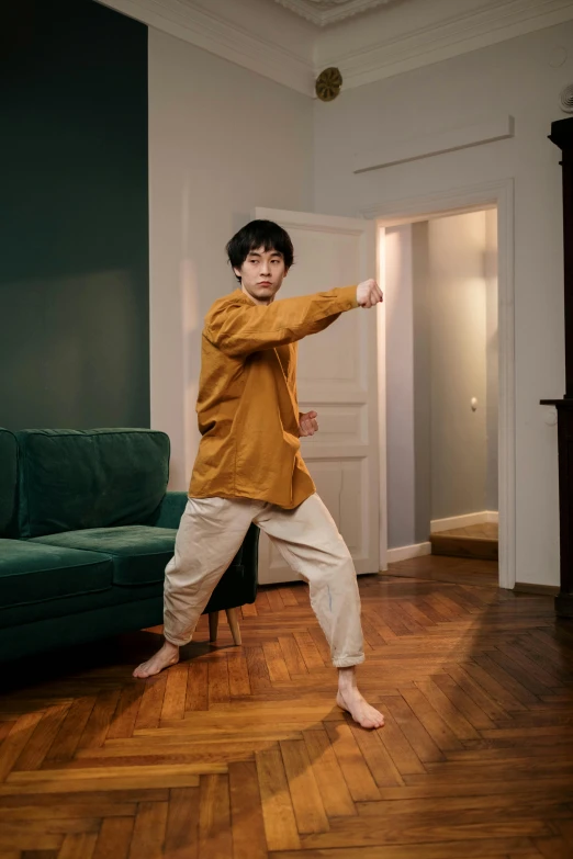 a man standing in a living room next to a couch, inspired by Ma Quan, pexels contest winner, shin hanga, fighting stance, wearing a baggy pajamas, with yellow cloths, standing in corner of room