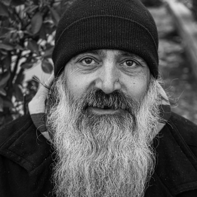 a black and white photo of a man with a long beard, a black and white photo, by Michalis Oikonomou, pexels contest winner, qajar art, he also wears a grey beanie, serene smile, holy aura, donald trump as a homeless man