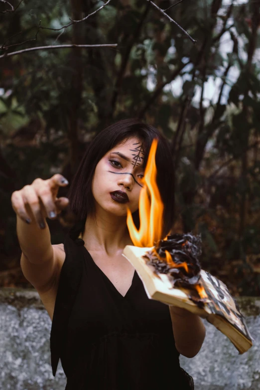 a woman holding a piece of wood with fire coming out of it, an album cover, by Lucia Peka, pexels contest winner, holding spell book, scary angry pose, instagram post, resin