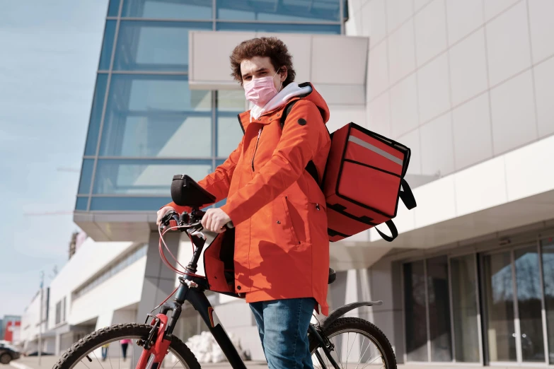 a man standing next to a bicycle wearing a face mask, trending on pexels, realism, orange jacket, delivering parsel box, cool red jacket, a man wearing a backpack