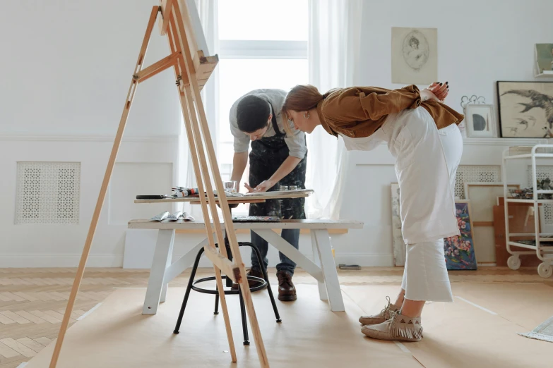 a woman and a child standing in front of a easel, inspired by artist, pexels contest winner, on a white table, artistic angle, on a wooden table, maintenance