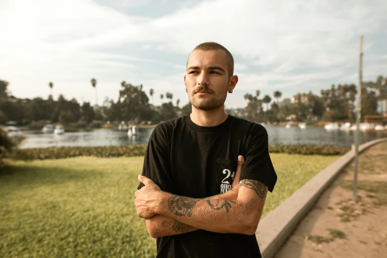 a man standing in front of a body of water, a portrait, unsplash, realism, lil peep, in a city park, buzz cut, rex orange county