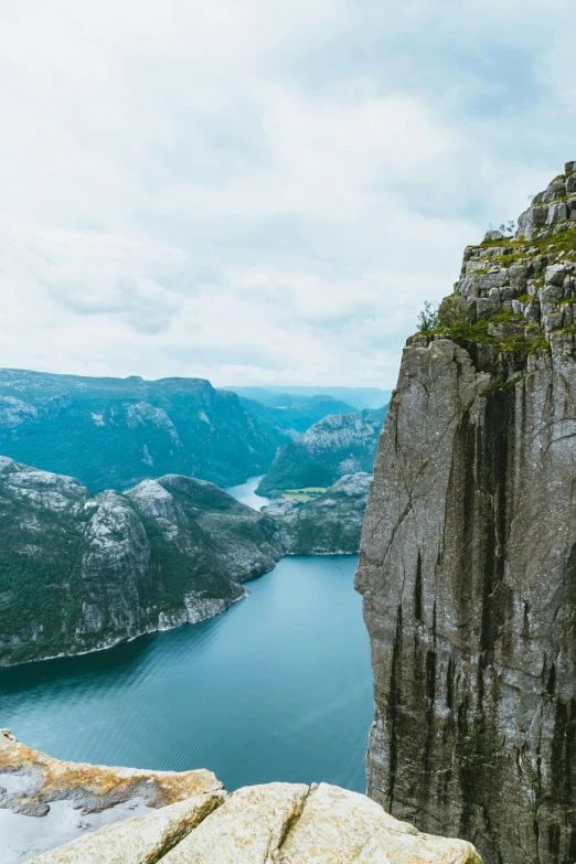 a man standing on top of a mountain next to a body of water, by Tom Wänerstrand, pexels contest winner, 4 k cinematic panoramic view, norwegian, rock climbing, sheer cliffs surround the scene