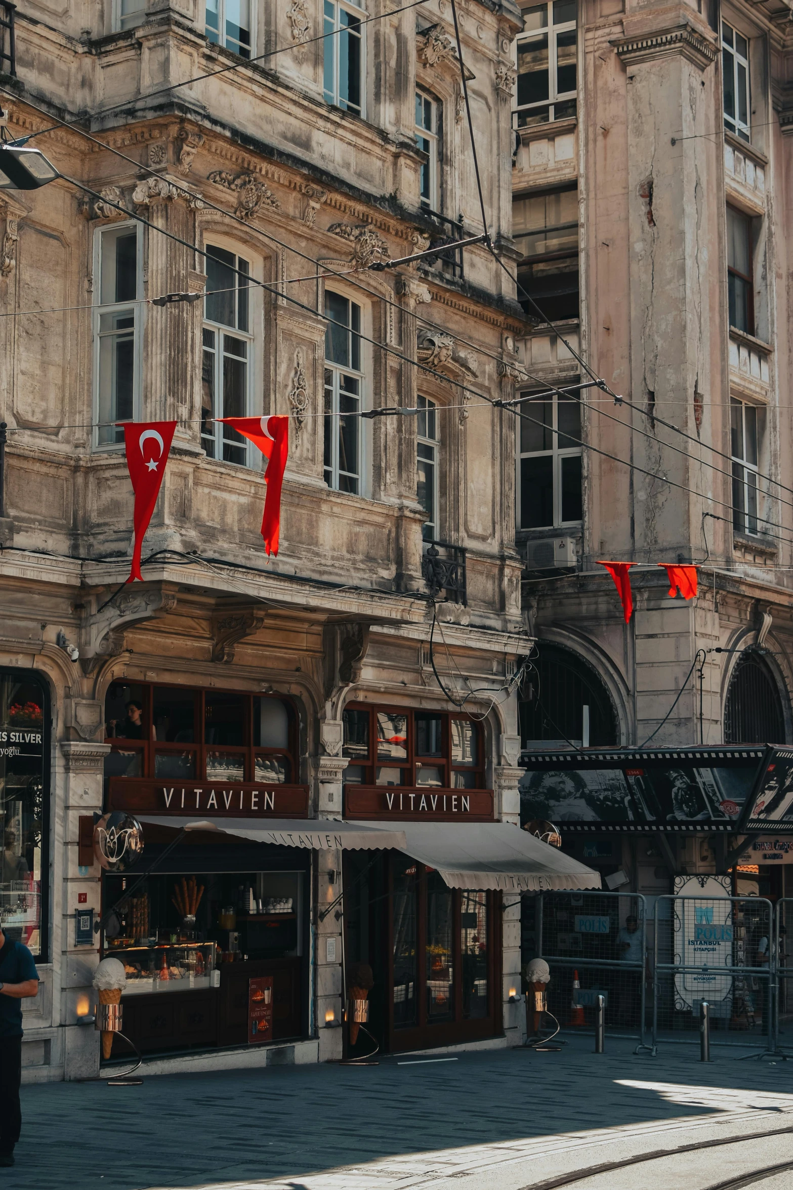 a bus driving down a street next to a tall building, a photo, pexels contest winner, art nouveau, red and black flags, ottoman empire, inspect in inventory image, old shops