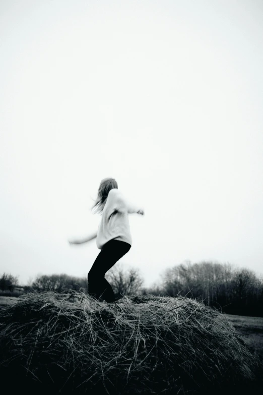 a woman standing on top of a pile of hay, a black and white photo, unsplash, conceptual art, girl running, blurry photo, winter season, music
