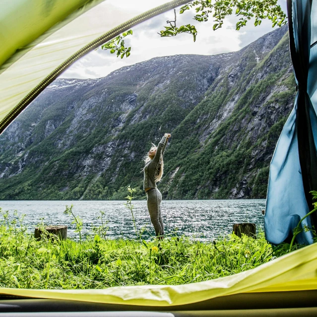 a man standing inside of a tent next to a body of water, by Caspar Wolf, pexels contest winner, arms stretched out, dhl yellow dhl van and the lake, norway, lush surroundings