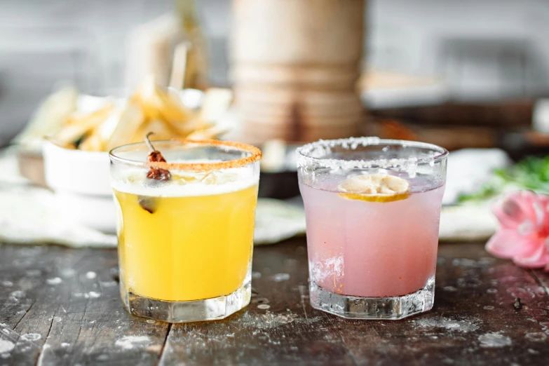 a couple of drinks sitting on top of a wooden table, by Carey Morris, unsplash, renaissance, pink and yellow, mexican, square, various posed