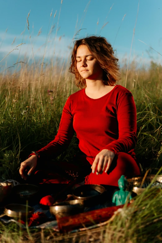 a woman sitting on top of a grass covered field, in a red dish, meditating, high-quality photo, promotional image