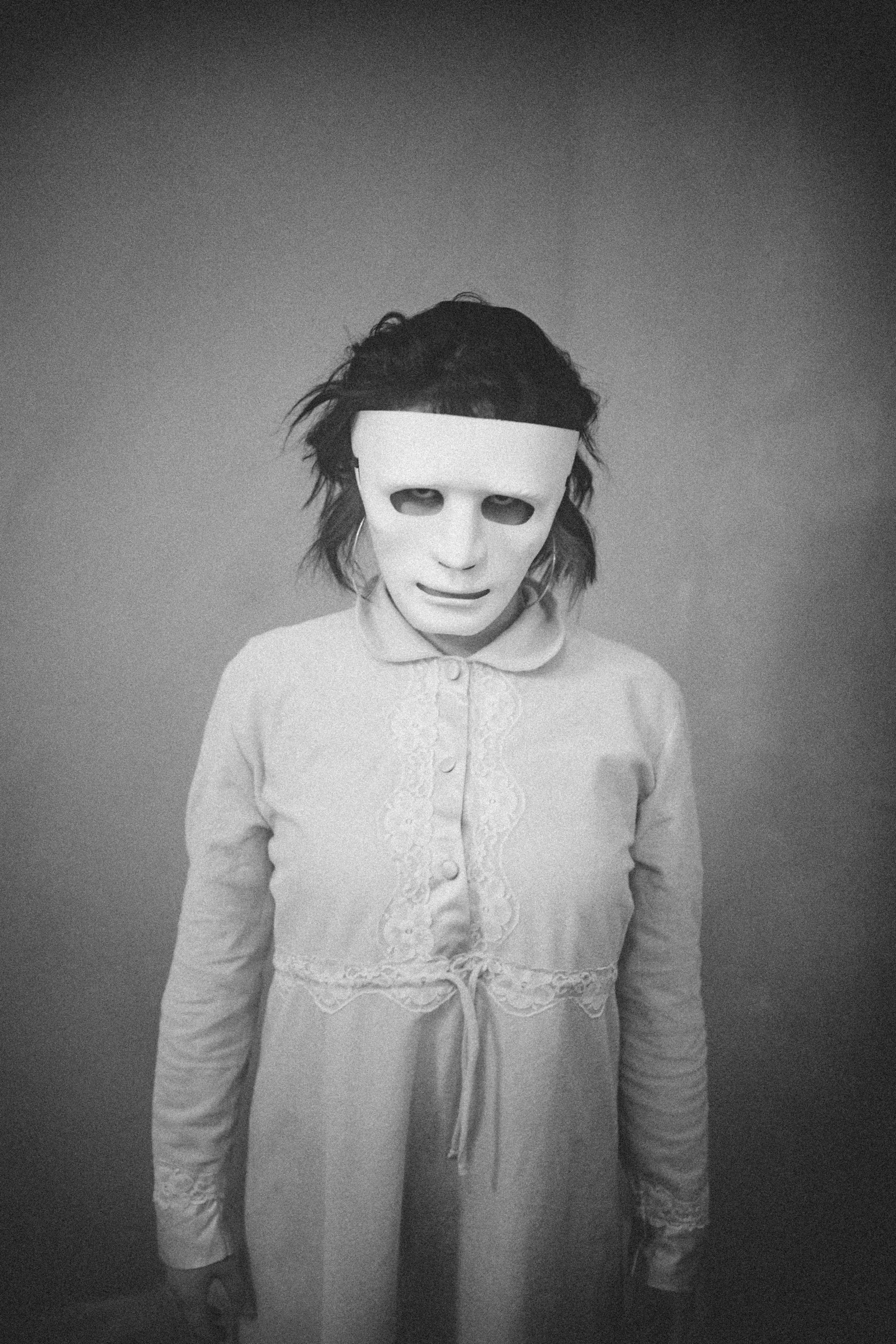 a black and white photo of a person wearing a mask, an album cover, inspired by Diane Arbus, tumblr, bauhaus, white clothes, eleven from stranger things, girl with white eyes, broken mask