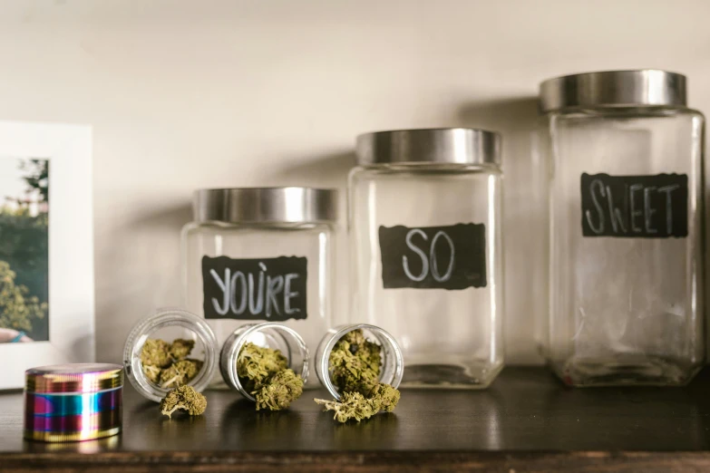 a wooden table topped with jars filled with marijuana, unsplash, graffiti, shelf, you're something special, glass jar, four legged