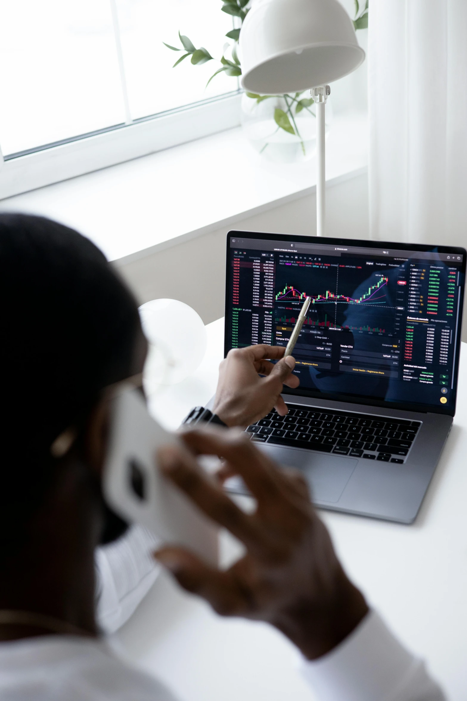 a man talking on a cell phone while sitting in front of a laptop computer, pexels, renaissance, waveforms on top of square chart, ( ( dark skin ) ), cryptocurrency, on a white table