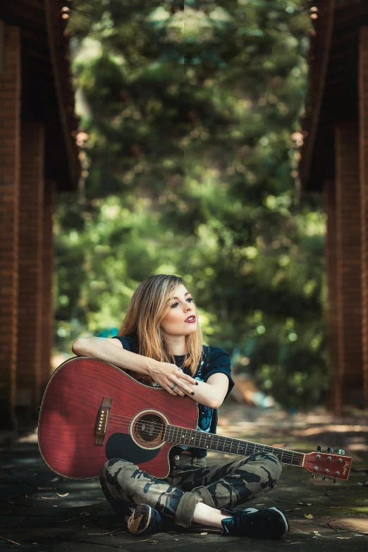 a woman sitting on the ground with a guitar, trees in the background, profile image, promotional image, portrait image