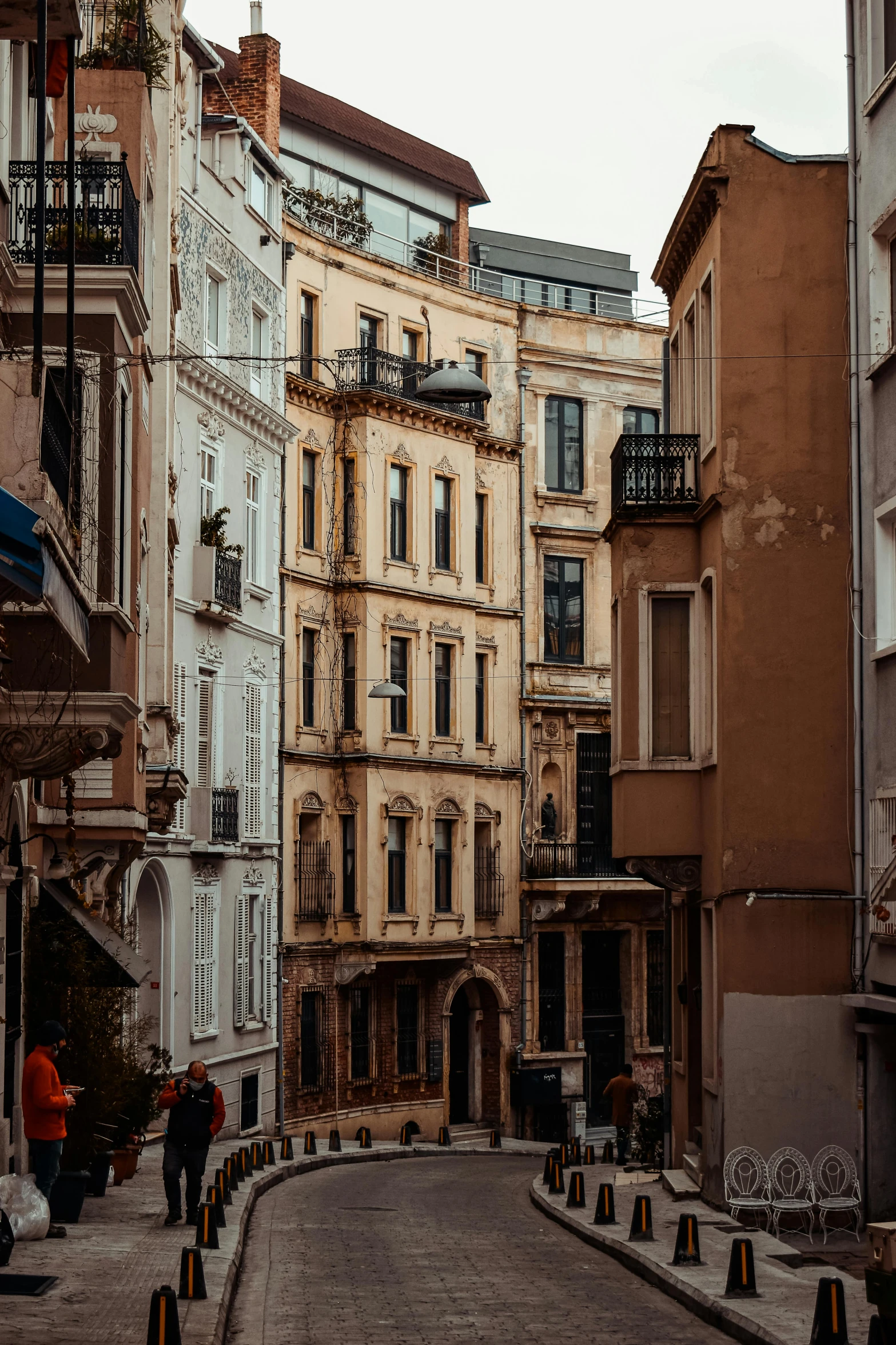 a couple of people walking down a street next to tall buildings, a picture, renaissance, istanbul, old apartment, beige, built on a steep hill