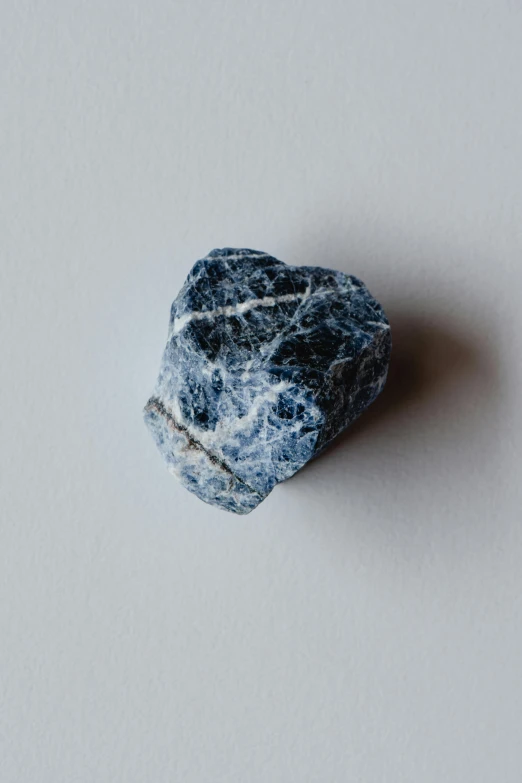 a rock sitting on top of a white surface, by Jessie Algie, unsplash, arabesque, navy-blue, dapple, made of stone, soda