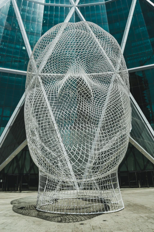 a sculpture of a head in front of a building, inspired by Buckminster Fuller, reddit, ultra detailed wire decoration, shrouded figure, detailed - face!!, person made out of glass