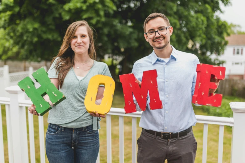 a man and a woman holding up letters that spell home, a colorized photo, pexels contest winner, letterism, cornell, midsommar color theme, headshot photo, casually dressed