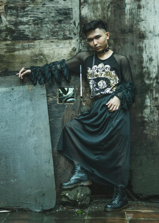 a man in a black dress leaning against a wall, an album cover, inspired by Oka Yasutomo, neo-dada, wearing ornate clothing, genderless, diesel punk, catalog photo