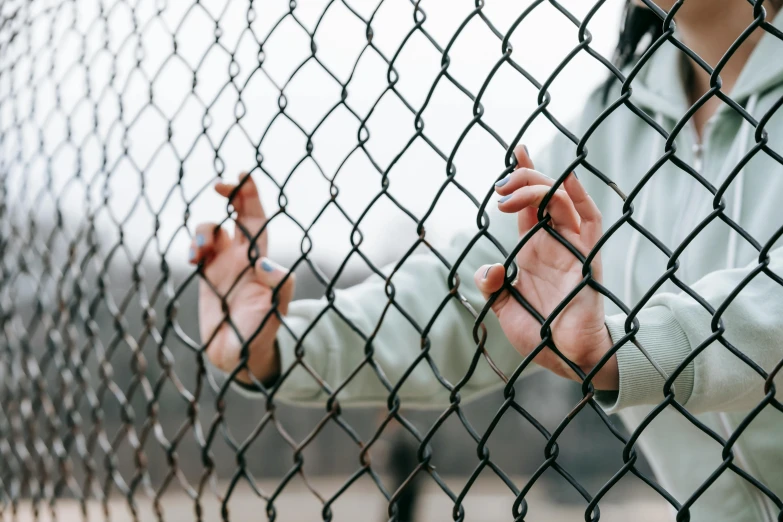 a woman standing behind a chain link fence, trending on pexels, detention centre, hands reaching for her, 🦩🪐🐞👩🏻🦳, recovering from pain