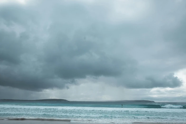 a man riding a wave on top of a surfboard, inspired by Thomas Struth, unsplash, minimalism, gloomy moody clouds, orkney islands, turquoise, standing on a beach