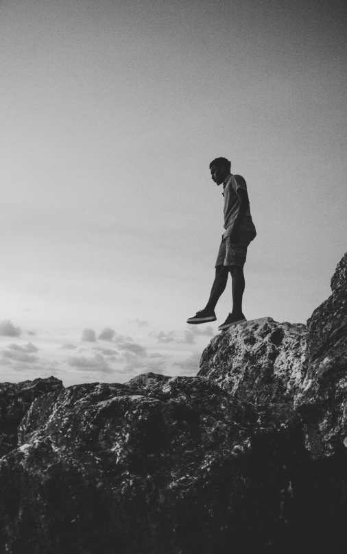 a black and white photo of a man standing on a rock, pexels, happening, black man, small steps leading down, teenage boy, floating in the sky