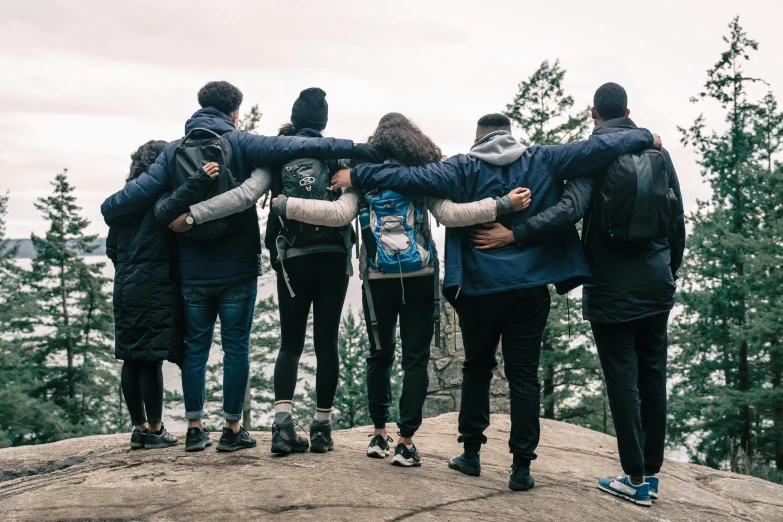 a group of people standing on top of a rock, wearing a blue hoodie, hug, on a canva, with a backpack