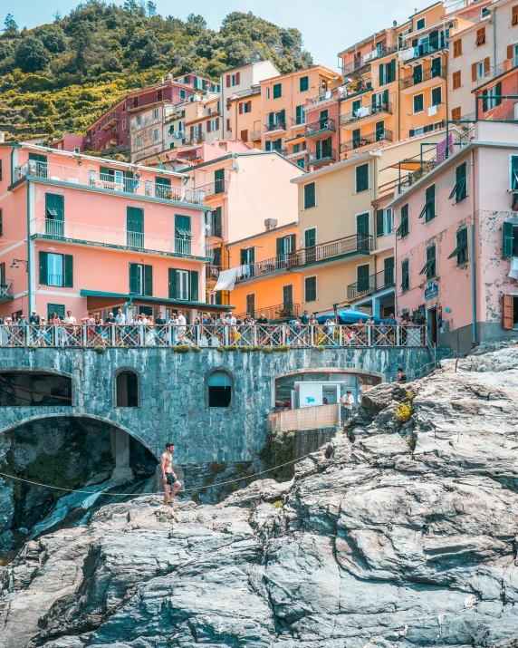 a group of people standing on top of a cliff next to a body of water, by Carlo Martini, pexels contest winner, renaissance, footbridges between houses, colorful tiled architecture, youtube thumbnail, small port village