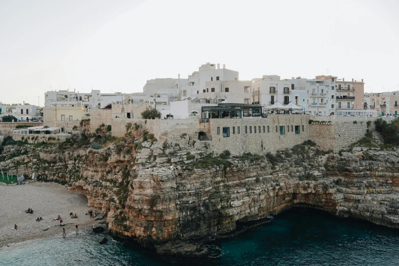 a group of people standing on top of a cliff next to a body of water, by Patrick Pietropoli, pexels contest winner, renaissance, whitewashed buildings, still from a wes anderson movie, conversano, a cozy