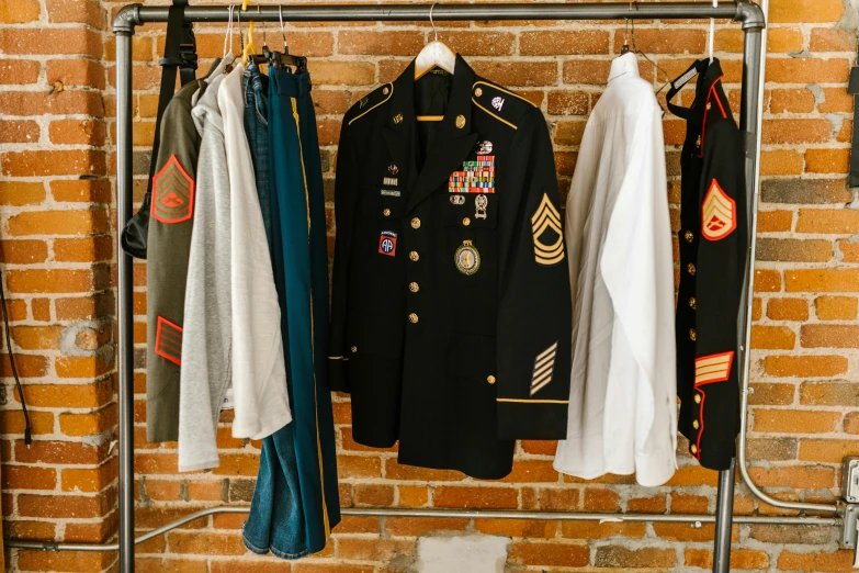 clothes hanging on a rack in front of a brick wall, private press, embroidered uniform guard, tech robes, military-grade, curated collections