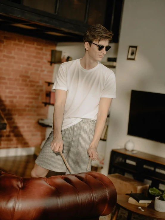 a man standing in a living room next to a couch, white shirt and grey skirt, giant wooden club, wearing shorts and t shirt, profile image