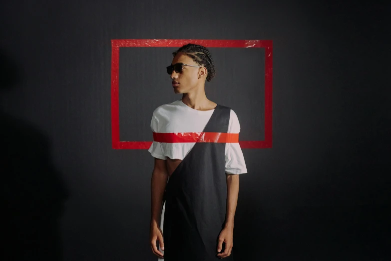 a man standing in front of a red frame, an album cover, inspired by Jean Malouel, pexels contest winner, antipodeans, ashteroth, black and red dress, on a black wall, model is wearing techtical vest