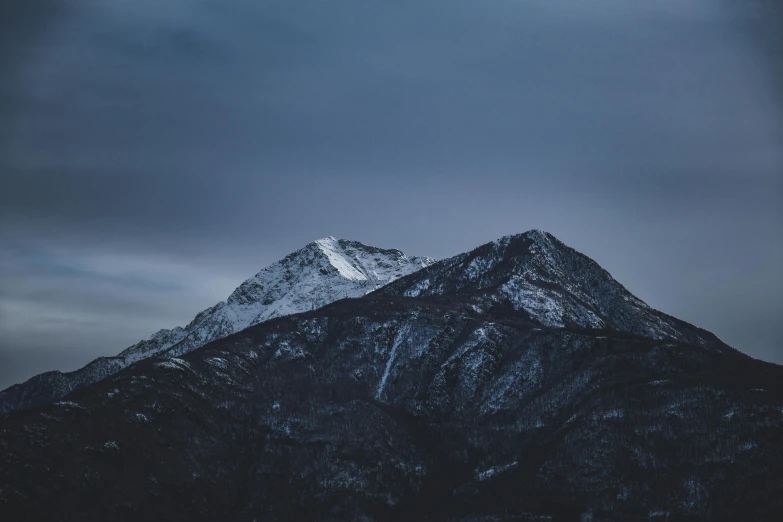 a mountain covered in snow under a cloudy sky, by Ryan Pancoast, unsplash contest winner, minimalism, ominous evening, clear dark background, viewed from a distance, multiple stories