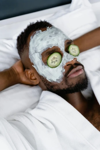a man laying in bed with cucumbers on his face, by Cosmo Alexander, trending on pexels, renaissance, black mask, with grey skin, wearing white pajamas, manicured