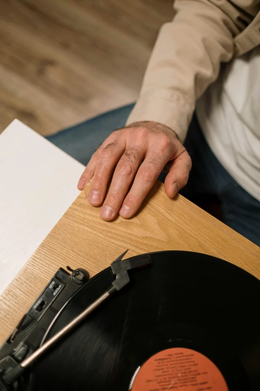 a person sitting at a table with a record on it, frail, touching, closeup of arms, still photograph