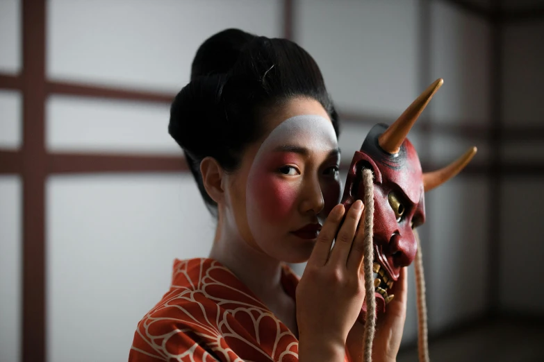 a woman holding a mask in front of her face, a portrait, inspired by Shunkōsai Hokushū, unsplash, human dressed as a bull, [ theatrical ], modelling, ad image