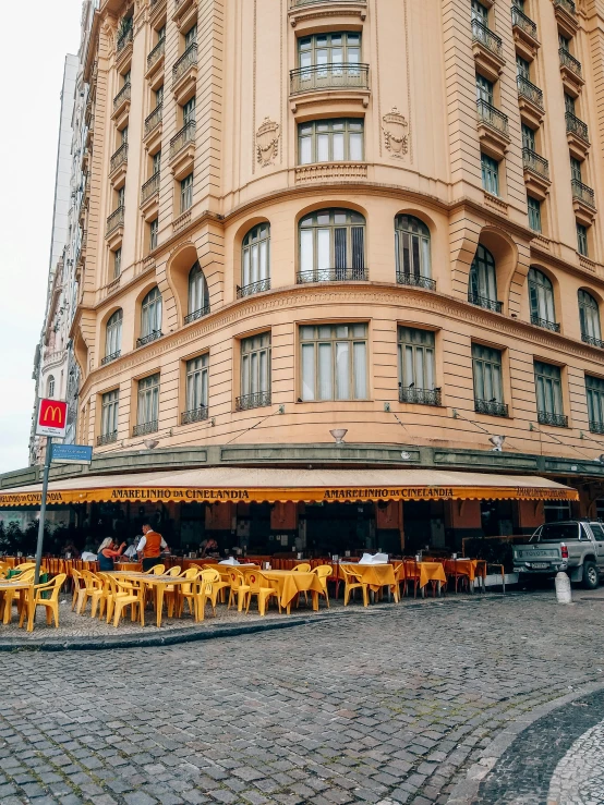 a building with tables and chairs in front of it, by Julia Pishtar, pexels contest winner, art nouveau, avenida paulista, yellow awning, high picture quality, low quality photo