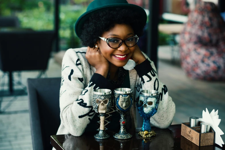 a woman sitting at a table with cups in front of her, a portrait, by Lily Delissa Joseph, pexels contest winner, afrofuturism, she wears harry potter glasses, voodoo”, exquisitely ornate, at a bar