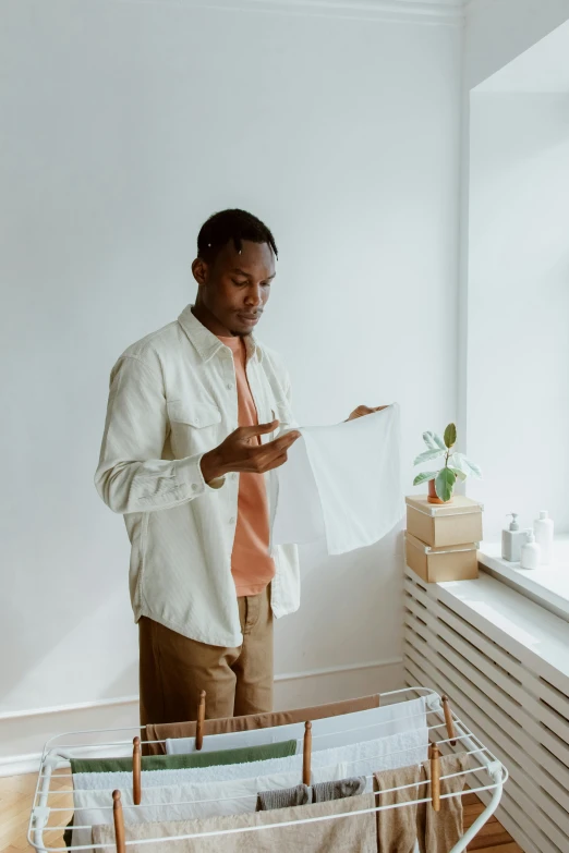 a man that is standing in front of a window, on high-quality paper, wearing a linen shirt, scanning items with smartphone, african canadian