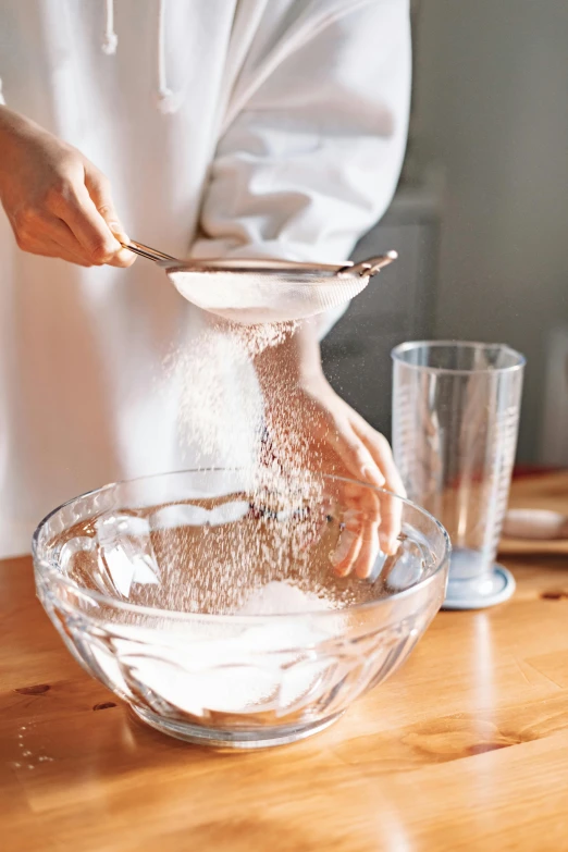 a person mixing ingredients in a bowl on a wooden table, inspired by Yukimasa Ida, glassware, powder, thumbnail, crispy