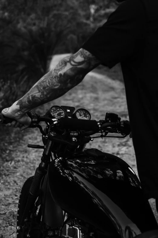 a man standing next to a motorcycle on a dirt road, a black and white photo, unsplash, realism, closeup of arms, tattooed, profile image, uploaded