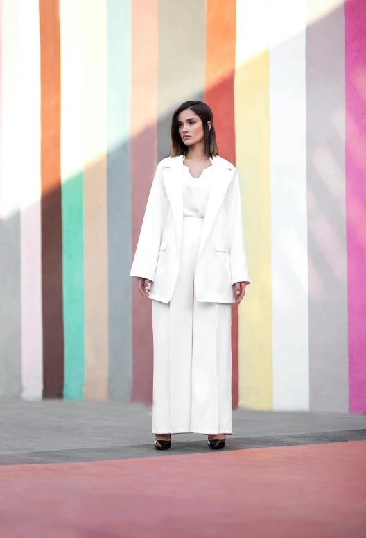 a woman standing in front of a colorful wall, an album cover, instagram, color field, wearing white suit, wears a long robe, like a catalog photograph, hila klein