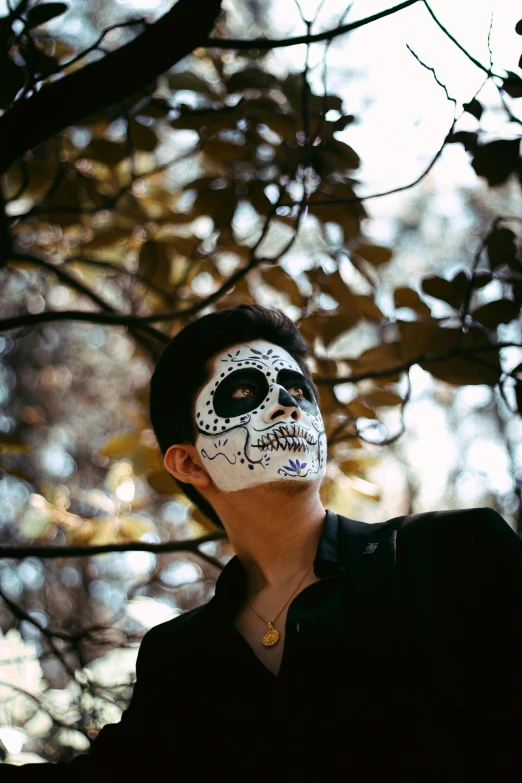 a man wearing a sugar skull mask standing in front of a tree, inspired by Taro Yamamoto, pexels contest winner, aestheticism, high cheekbones, ( ( ( skeleton ) ) ), ryan jia, mime